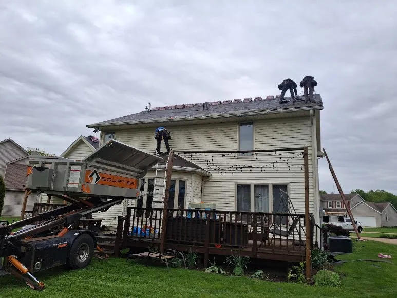 Hershberger Brothers Roofing crew on the roof of a two-story home, with the trailer in the driveway