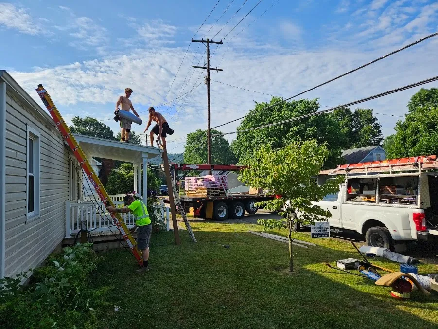Hershberger Brothers Roofing crew carrying shingles up a ladder, with the work truck in the driveway